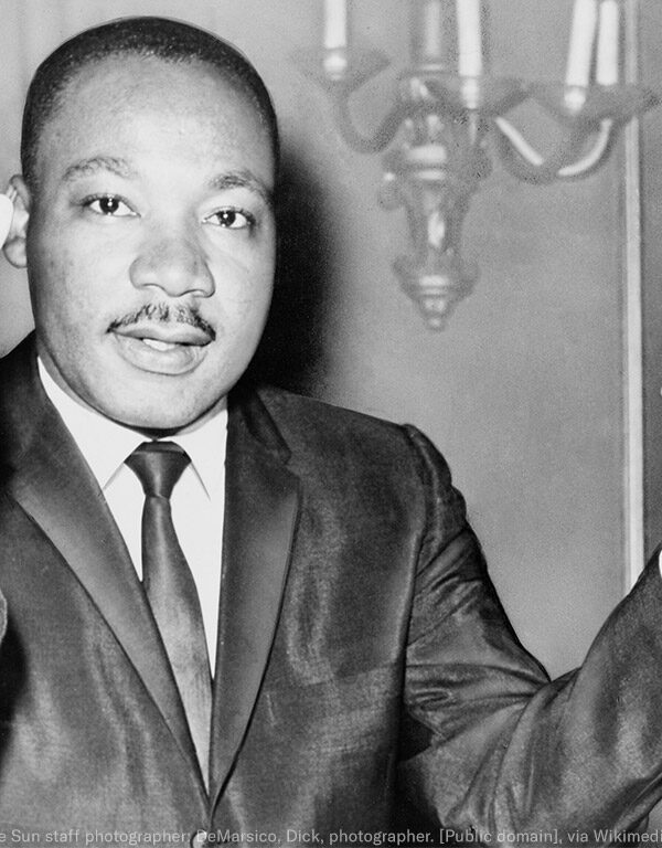 Rev. Martin Luther King, head-and-shoulders portrait, seated, facing front, hands extended upward, during a press conference