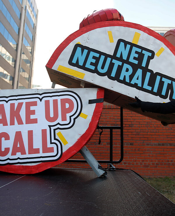 Woman helps to dismantle a large alarm clock display that reads "Net Neutrality Wake Up Call" from the stage after a protest in front of the FCC in Washington, DC.