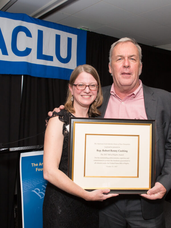 Devon Chaffee and Renny Cushing hold an award certificate with an ACLU banner in the background