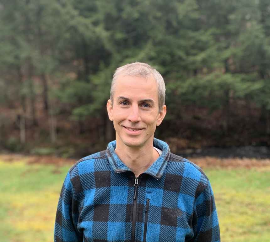 Headshot of Frank Knaack, who is standing in front of green trees wearing a plaid jacket