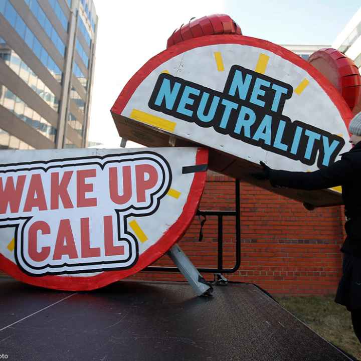 Woman helps to dismantle a large alarm clock display that reads "Net Neutrality Wake Up Call" from the stage after a protest in front of the FCC in Washington, DC.