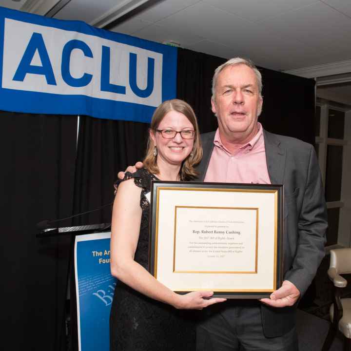 Devon Chaffee and Renny Cushing hold an award certificate with an ACLU banner in the background